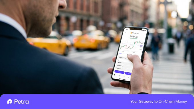 In this image, there is a man standing next to a busy street while he holds up his cell phone displaying some information about currency trading services called Petron. The man seems to be looking at the data displayed on his phone screen. The background features various elements from an urban environment, such as cars and people walking around, adding to the overall setting of the scene. There is also a website link provided in the image description that points towards another source for more information about Petron trading services.