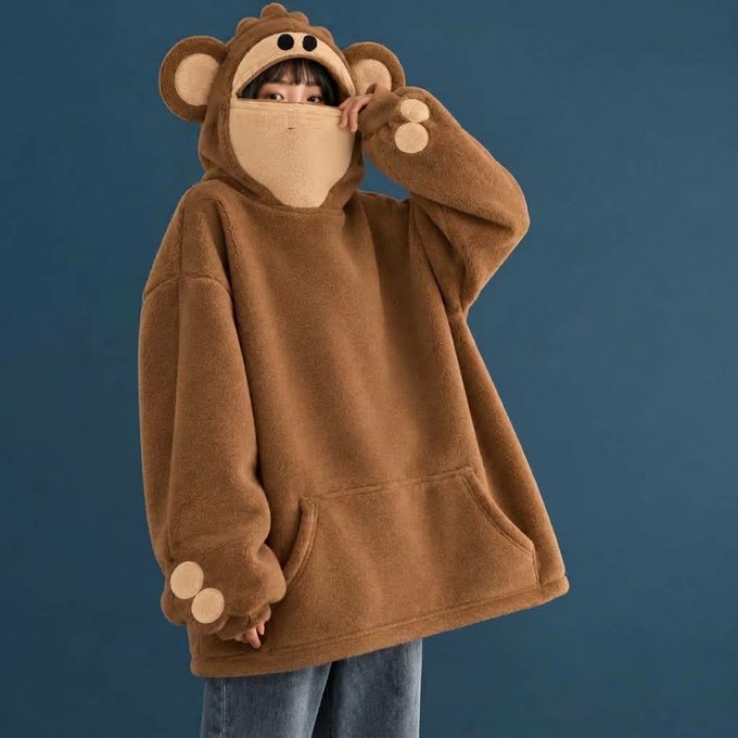 A person modeling a cozy, oversized brown fleece hoodie designed as a hooded bear costume with bear ears and paw mittens.