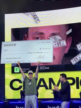 The image shows TraderMayne holding up a large novelty check from PayPal for $25,000, while another person tosses fake cash into the air, celebrating his victory as a champion at what appears to be an event in a stadium with a jumbotron in the background. This directly relates to the post praising TraderMayne as the "goat" (greatest of all time) and "True Vet," highlighting his impressive earnings and competitive success.