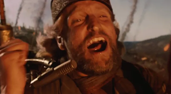 A close-up still shows a rugged, bearded man in a cap yelling or singing into a vintage microphone in a dusty outdoor setting. The image contains no readable text or numbers, and the caption “Bro shorting the market 1000x rn” frames the exaggerated expression as a humorous reaction to market-trading chaos.