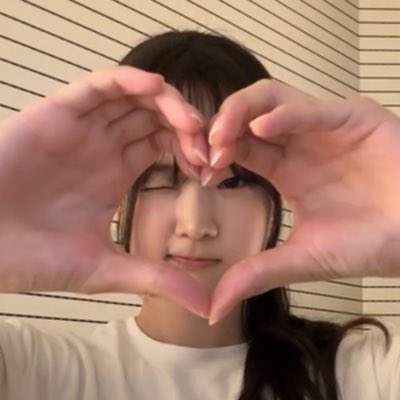 A young woman forms a heart shape with her hands in front of her face.