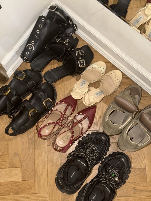 A stylish assortment of shoes—including Steve Madden sneakers, buckle-adorned boots, and various sandals—sprawled across a wooden floor, humorously capturing the dilemma of a fashion-conscious girl navigating Solana Summit in Serbia, where practicality and style collide.