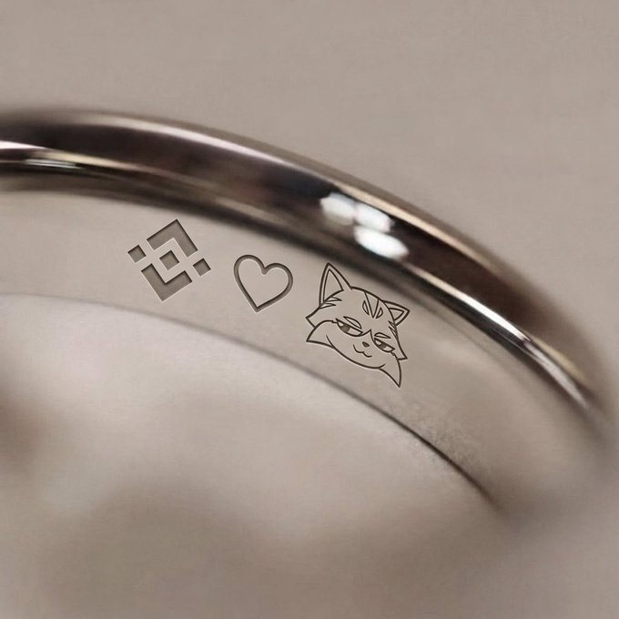 A close-up of the inside of a silver ring engraved with three symbols: a geometric pattern, a heart, and a fox face.