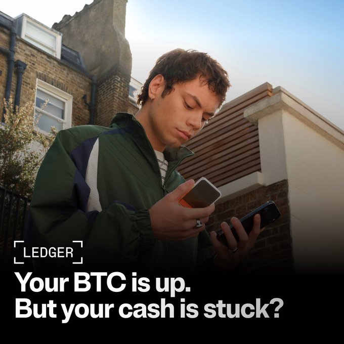 A young man in a green jacket stands on a residential street, intently looking at two smartphones in his hands. Overlaid text reads "LEDGER - Your BTC is up. But your cash is stuck?" The image visually represents the post's theme of trading crypto actively while keeping private keys secure offline, highlighting the frustration of having valuable BTC but difficulty accessing its liquidity.