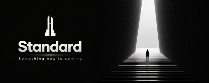 A sleek, minimalist black banner with the text "Standard — Something new is coming," alongside a silhouetted figure walking up illuminated steps toward a bright opening, evoking a sense of anticipation and mystery for the Standard project's upcoming reveal.