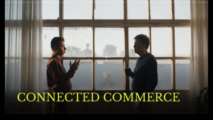 A cinematic scene showing two men silhouetted against a large window with a cityscape view, overlaid with the yellow text 'CONNECTED COMMERCE'.