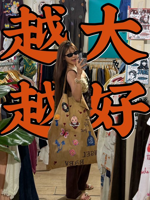 A woman taking a mirror selfie in a vintage clothing store, holding a canvas tote bag covered in colorful patches and embroidery; large orange Chinese characters are overlaid on the image.