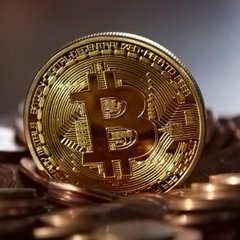A physical Bitcoin token featuring the iconic "₿" symbol and circuit-like design rests atop a pile of similar gold-colored coins, visually representing the cryptocurrency's role as the central subject of the article about AI potentially simplifying Bitcoin adoption through wallets and onboarding.