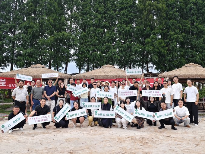 Group photo of a corporate event on a beach with thatched umbrellas in the background; attendees hold various signs including 'EVE Group' branding and slogans about 'creativity' and 'valuing time'.
