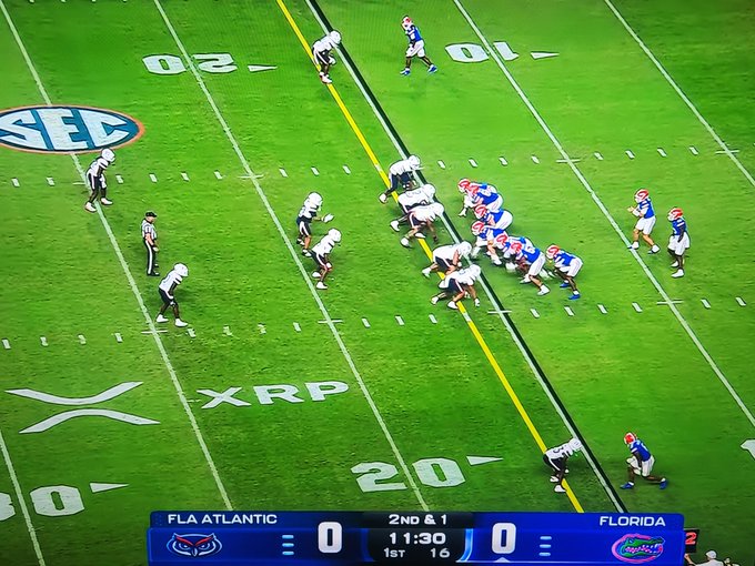 An SEC football game between Florida Atlantic and Florida is underway, with the score tied 0-0, 11:30 remaining in the 1st quarter on a 2nd & 1. The XRP logo is prominently displayed as an on-field sponsor at midfield, visually reinforcing the post's claim of XRP's widespread brand visibility.
