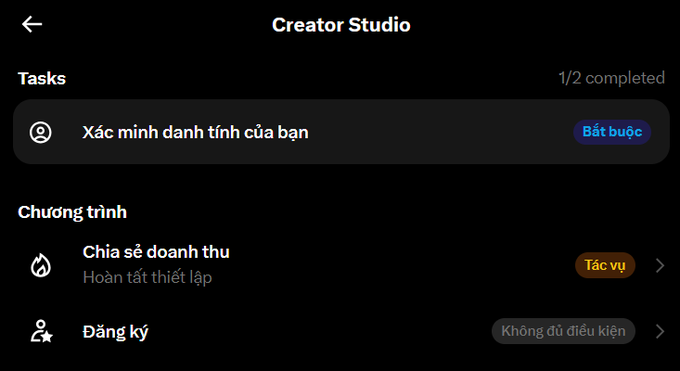A screenshot of the Creator Studio interface in Vietnamese, showing 'Tasks' (1/2 completed) with 'Xác minh danh tính của bạn' (Verify your identity) marked as 'Bắt buộc' (Required), and a 'Chương trình' section listing 'Chia sẻ doanh thu' (Revenue sharing) and 'Đăng ký' (Sign up) options.