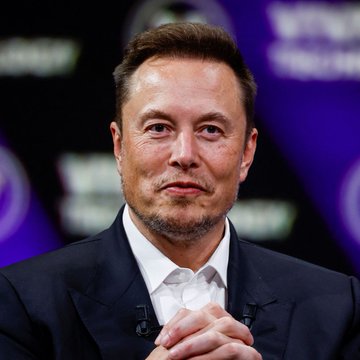 Elon Musk sits with his hands clasped together, looking composed and thoughtful during what appears to be a formal event or interview setting. His contemplative pose visually complements the post's discussion of his measured commentary on quantum computing limits and Palmer's theory about qubit scalability.