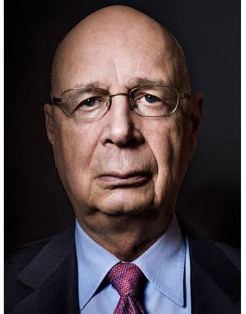 A formal portrait of an older bald man with glasses, wearing a grey suit and blue shirt with a red patterned tie.