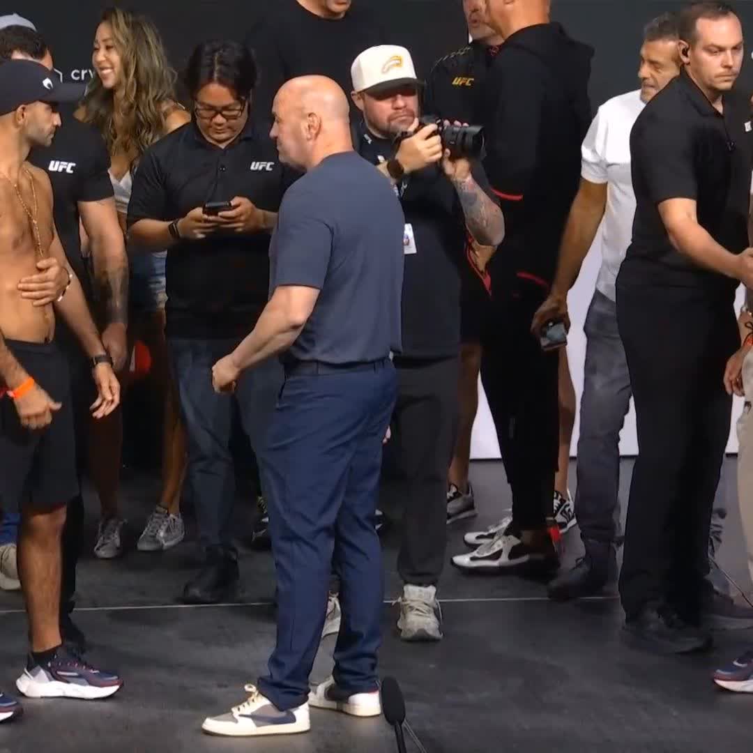 UFC President Dana White stands between Giga Chikadze (left, shirtless with a chain) and a member of Bruno Silva's corner during a pre-fight face-off ahead of UFC 331 at Crypto.com Arena, as event staff in UFC-branded shirts and a photographer observe the staredown.