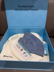 An open blue box from Ripple displays the text 'Turning Crypto into Everyday Finance', containing folded clothing and a small tube of lotion.