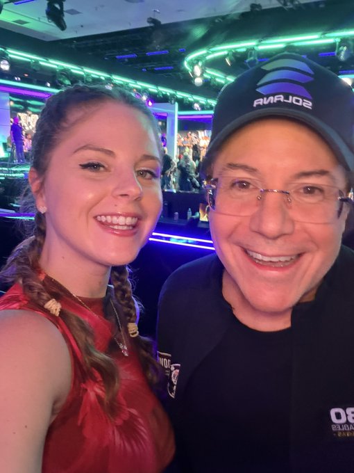 A young woman with braided hair smiles alongside a man wearing a "SOLANA" cap and glasses, likely at the WSOP Solana poker match she mentioned, with the man possibly being poker champion Jamie Gold as referenced in her shoutout.