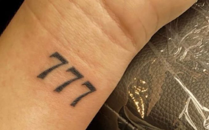 A close-up of a wrist tattoo featuring the numbers "777" in a bold, gothic-style font.