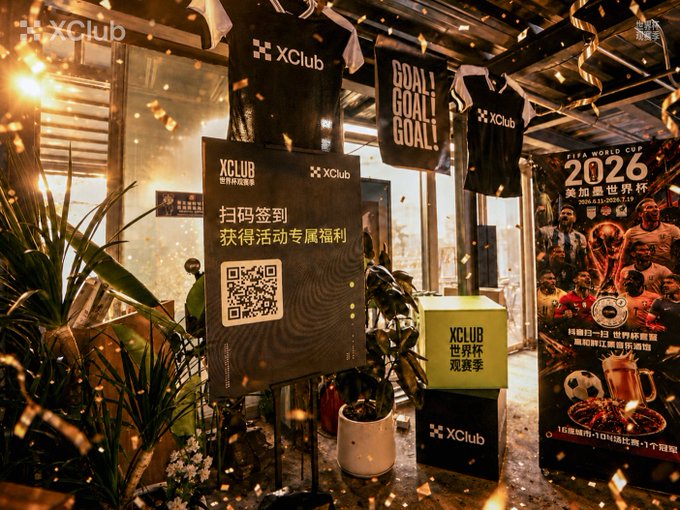 XClub World Cup 2026 promotional event space with FIFA World Cup posters, merchandise including 'GOAL GOAL GOAL' jerseys, a QR code check-in sign in Chinese, and confetti falling.