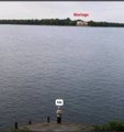 A photo taken from a shoreline looking out over a wide body of water towards a distant building with a red sign that appears to read "Marlboro".