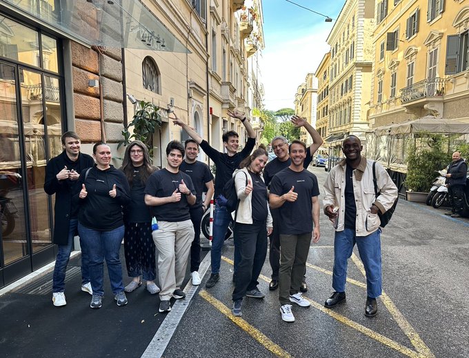 A group of people, possibly colleagues, are posing together on a city street with their thumbs up and arms raised. The image doesn't relate to the caption, as the caption discusses Bitcoin miners and a metaprotocol, while the image shows a group of people without any Bitcoin miners or a metaprotocol visible.