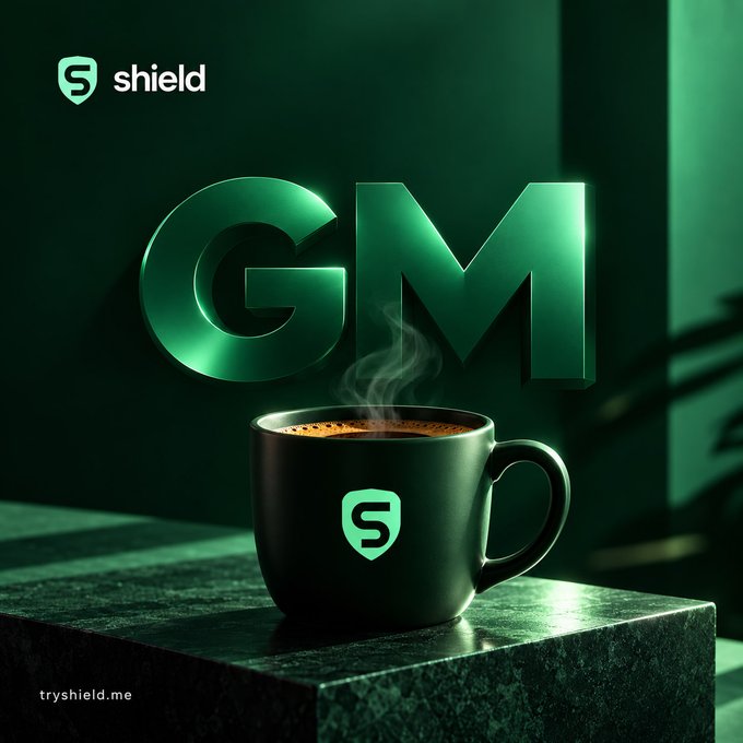 A promotional advertisement for 'GM' featuring a steaming black coffee mug with the 'shield' logo and 'S' emblem on a green-tinted surface, with 'shield' branding in the upper left and 'try shield.me' text in the bottom left.
