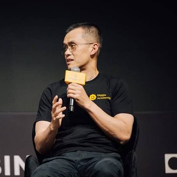 Binance founder Changpeng Zhao (CZ), wearing a black t-shirt with the yellow Binance logo, speaks into a microphone while seated on stage, discussing market conditions. His commentary on potential bear market trends despite available investment capital directly relates to the post's quote about the current state of the crypto market.