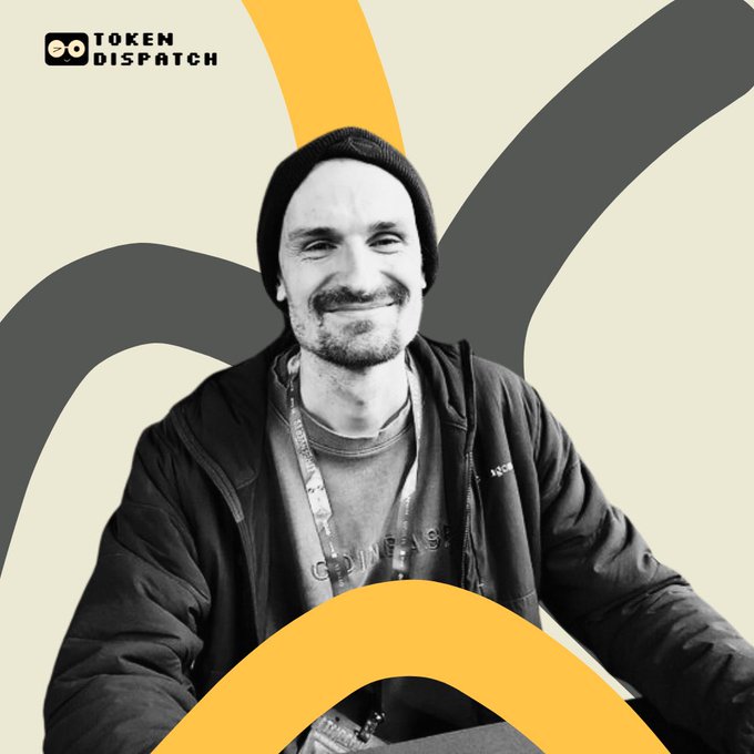 A black and white photo of a smiling man in a beanie and hoodie with 'TOKEN DISPATCH' branding in the upper left corner.