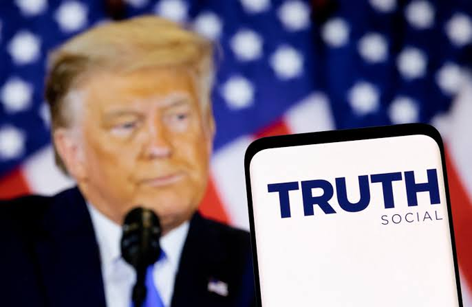 The image shows Donald Trump with a smartphone displaying the "TRUTH SOCIAL" logo, relevant to news about Trump Media's significant crypto losses.