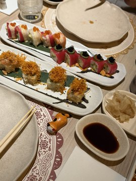 A dining table displays an assortment of sushi, including rolls topped with avocado and red tuna, alongside small dishes of soy sauce and pickled ginger.