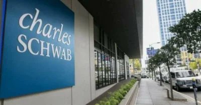 The image features a large Charles Schwab sign outside of their office building. The text on the sign reads "Charles Schwab Launches 24/7 Bitcoin, Ether, Solana, XRP Futures Trading". This suggests that the company is launching new trading options for digital assets such as Bitcoin and Ether, along with traditional fiat currency like dollars and euros. Additionally, they are also offering spot crypto options to financial advisors who want to invest in these digital assets. The image shows a street scene with cars parked on the side of the road and trees nearby, indicating that this is likely taking place in an urban setting.