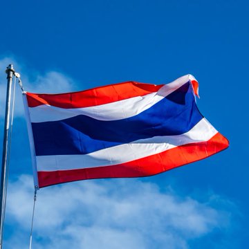 The Thai national flag, featuring red, white, and blue horizontal stripes, waves against a bright blue sky with scattered clouds. This image relates to the post as Thailand's SEC is seeking public input on regulations for Bitcoin and Ether ETFs, marking a step toward potential crypto investment offerings in the country.