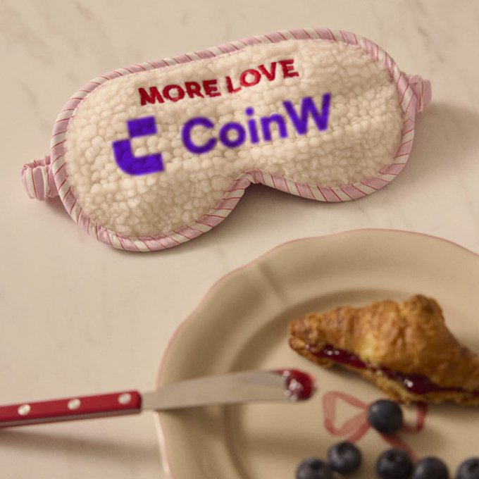A plush sleep mask with "MORE LOVE" and the "CoinW" logo sits on a marble surface beside a plate with a croissant, jam, and blueberries, complementing the post's cheerful "GM 美味相伴，元气出发" (Good morning, delicious companions, start with energy) vibe by visually pairing the brand's restful accessory with a wholesome breakfast.