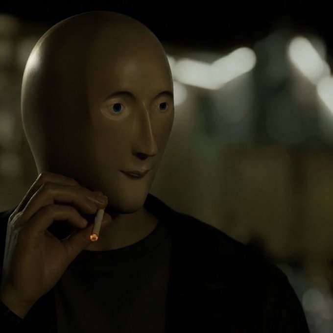 A surreal, unsettling figure wearing a smooth, featureless white mask with painted eyes and lips, holding a lit cigarette in a dark, dimly lit environment.