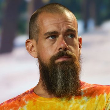 A bearded man with a shaved head, wearing an orange and yellow tie-dye shirt, looks off to the side with a contemplative expression. The image likely depicts Jack Dorsey, the founder of Block (formerly Square), whose company is seeking a U.S. national bank charter to offer federally regulated custody for digital assets including Bitcoin.
