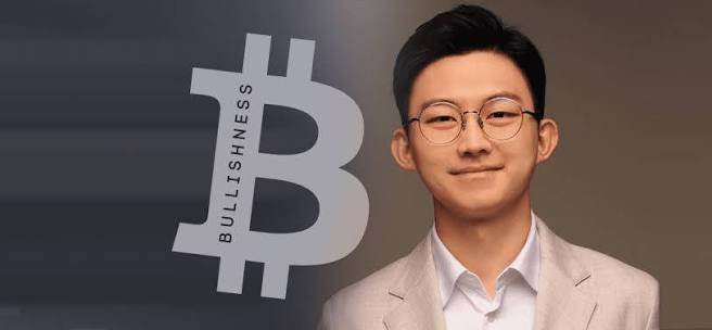 An image showing an AI-generated illustration of a young man with glasses and a beige suit jacket against a dark gradient background, with a large grey Bitcoin logo featuring the word "BULLISHNESS" written vertically across it on the left side.

**Connection to the post:** The Bitcoin "BULLISHNESS" graphic visualizes the optimistic market sentiment described in the caption, where Ki Young Ju's statement from CryptoQuant has sparked excitement among traders, suggesting a bullish outlook on the cryptocurrency market.