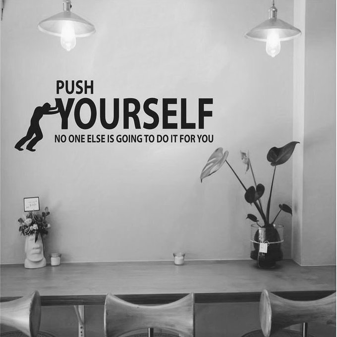 Black and white photo of an interior space featuring a wall decal that reads 'PUSH YOURSELF NO ONE ELSE IS GOING TO DO IT FOR YOU' alongside a silhouette of a person pushing.