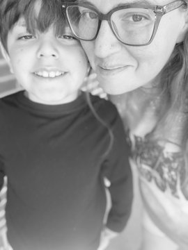 A black and white selfie showing a smiling woman wearing glasses posing closely with a young boy.