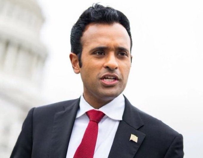 The image features a man dressed in a suit and tie standing outside of a building with the Washington Monument visible behind him. The man appears to be speaking or giving a speech, as indicated by his facial expression. In the background, there are two flags - one representing the United States and another symbolizing the British Commonwealth. The text "BREAKING: BILLIONAIRE VIVEK RAMASWAMY'S STRIVE JUST BOUGHT $85,000,000 WORTH OF BITCOIN" suggests that the man is a successful businessman who has recently made a significant monetary investment in Bitcoin.