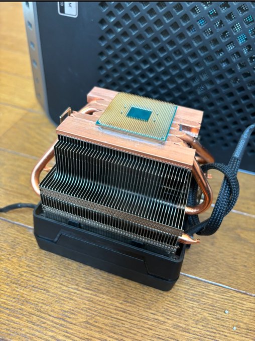 A CPU cooler with copper heat pipes and aluminum fins sitting on a wooden surface, with a small CPU chip placed on top.