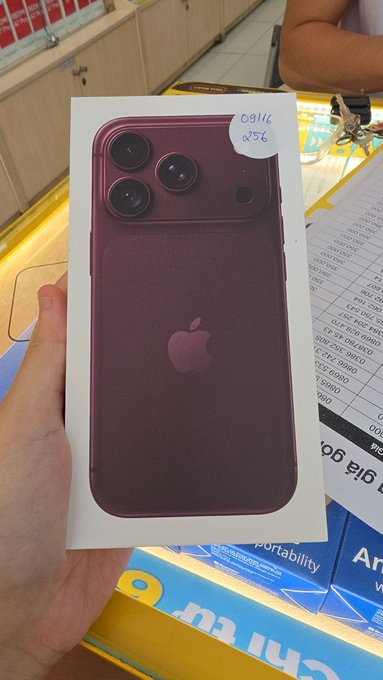 A hand holds a white box for a purple Apple iPhone, with a handwritten label reading "09116 8256".