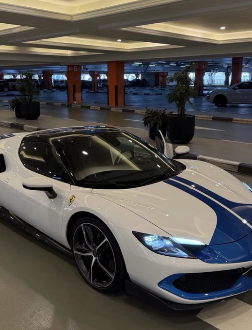 A white and blue Ferrari sports car is parked in an underground garage marked with an orange 'B4' pillar, with other vehicles visible in the background.