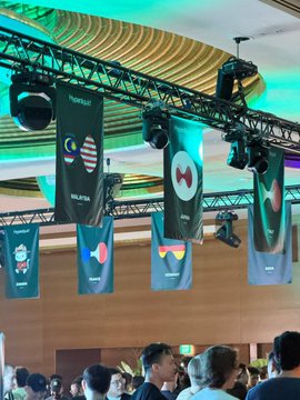 An indoor convention space featuring hanging banners for various cryptocurrency projects including 'vechain', 'MAJOR', 'Peapods Finance', and 'Peapods', suspended from a ceiling rig with spotlights.