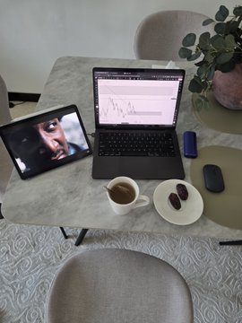 A laptop displaying charts sits alongside a tablet showing a video call, a coffee cup, and a small plate with treats on a marble table—visually capturing a focused work or study session that pairs with the caption "Lock in: Next 365 days can change the game." The setup conveys discipline and dedication, reinforcing the message of committing to a year of effort for transformation.
