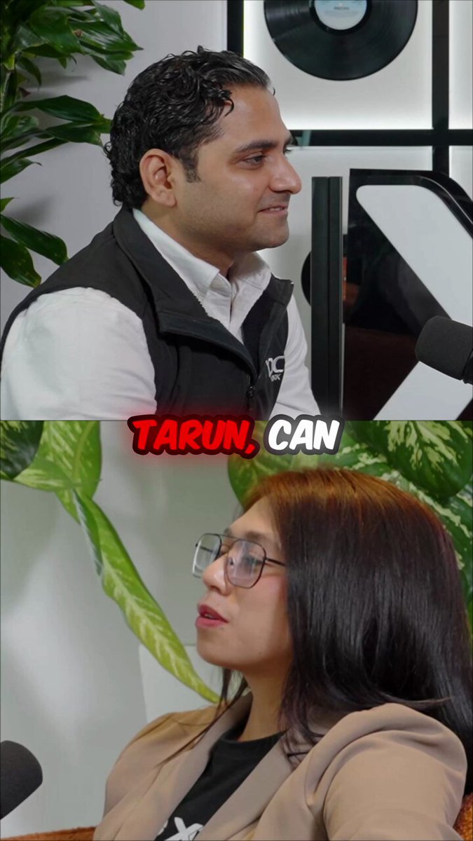 The image shows a man wearing glasses and a black vest, sitting next to a woman who has long hair and is wearing glasses as well. They are both looking at something off-camera. The background of the image features a plant, which adds some greenery to the scene. The caption below the image reads "Tarun, Can".