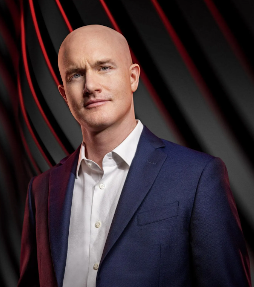 A bald man in a navy blue suit and white dress shirt poses confidently against a dark background with red lighting accents. The image appears to depict Brian Armstrong, CEO of Coinbase, as referenced in the accompanying post about his bullish Bitcoin price prediction.