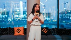 A woman with long dark hair, wearing a white outfit, speaks into a microphone on a stage decorated with Binance-branded cushions against a city skyline backdrop, tying into the post's celebration of the MENA community marking Binance's 9th anniversary together.