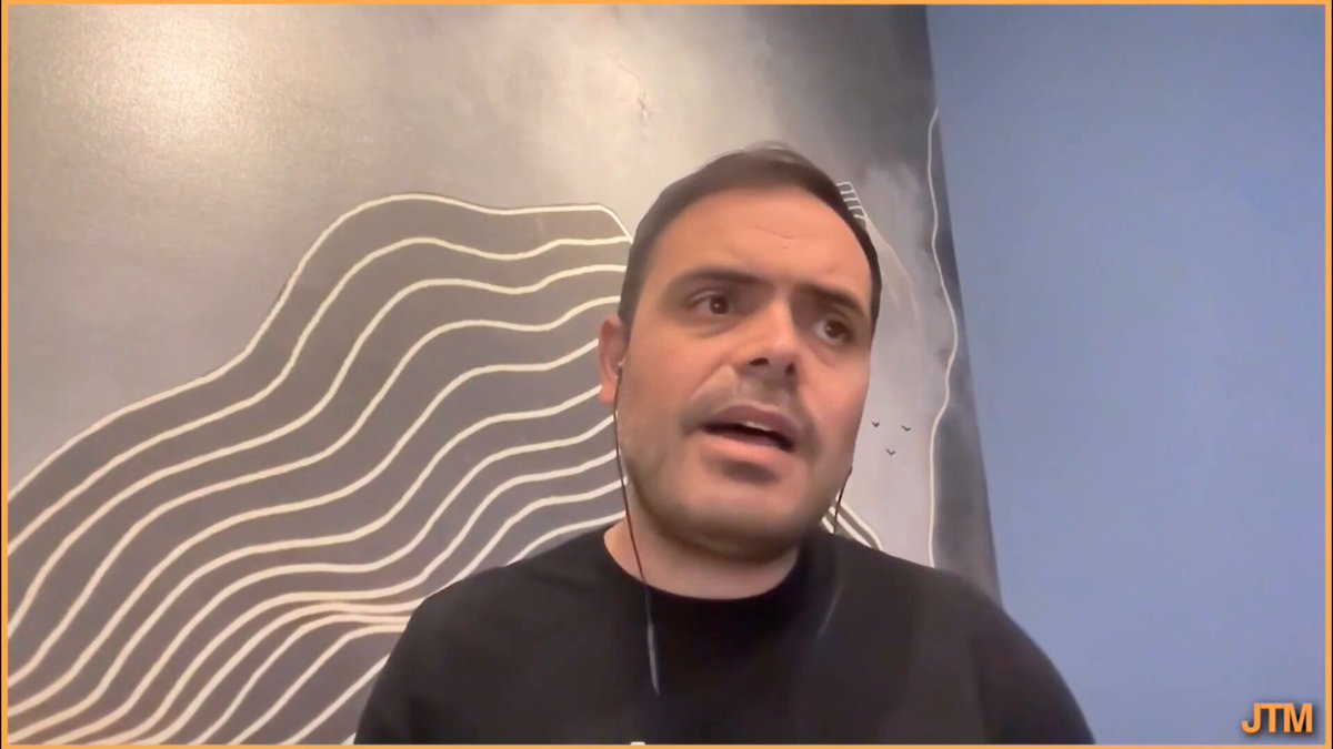 The image shows a man wearing a black shirt with white lines on his neck talking into a microphone during an online meeting or webinar, possibly discussing a project like Libra. The background of the image features a blue wall with white lines running across it. The caption provided in the image suggests that the man is sharing information about a project related to the creation of a new type of cryptocurrency called @sui network, which has been developed by @b1ackd0g and @kostascrypto. This project aims to provide a secure and transparent platform for users to manage their digital assets. The image also includes an orange watermark that reads "JTM" at the bottom right corner of the frame.
