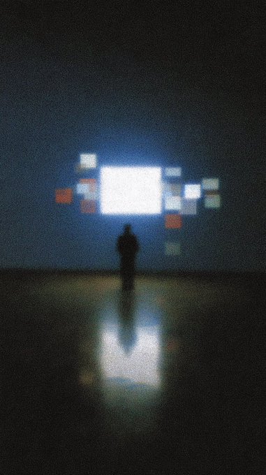 A silhouetted figure stands in darkness facing a cluster of glowing white and red rectangular lights that reflect on the wet ground.
