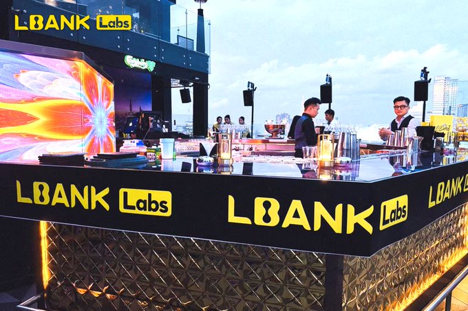 A vibrant rooftop bar scene features bartenders serving drinks behind a counter branded with yellow 'LBANK Labs' logos, alongside a glowing, colorful digital display.