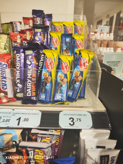 A convenience store shelf display featuring Cadbury Dairy Milk and Whole Nut Barsista chocolate bars with prices labeled 1.00 and 3.75, photographed with a Xiaomi 12T Pro.